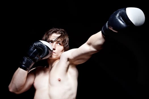 Young caucasian man boxing with gloves on black background