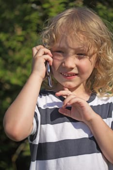Young attractive blond boy with long hair is calling by phone outdoors