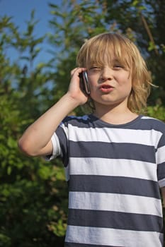 Young attractive blond boy dressed in a striped shirt is calling outdoors