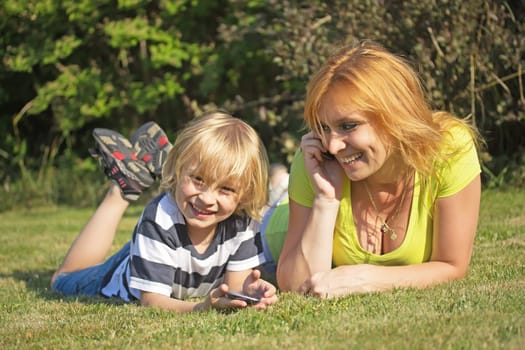 Laughing mother with her blon hair son lying on the lawn and telephone.