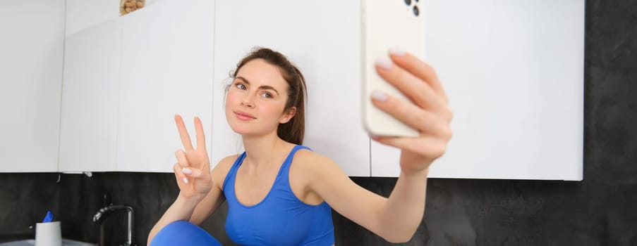 Fit and healthy young sports woman, showing peace sign, taking selfie in activewear, fitness blogger making photos for social media in her activewear.