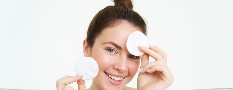Beauty and cosmetics. Young smiling woman washing her face with cotton pads, using facial cleanser, looking happy at camera.