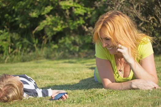Smiling mother with her blond hair son in the garden. Blond boy is lying on his bed.