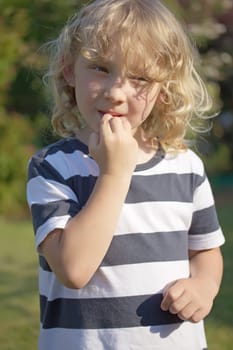 The blond boy in a striped shirt is biting his nails. Vertically.