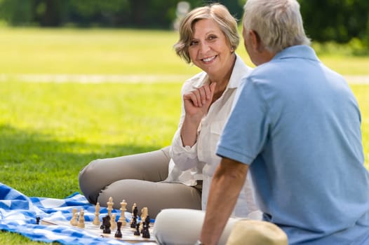 Senior wife and husband playing chess on blanket summer park