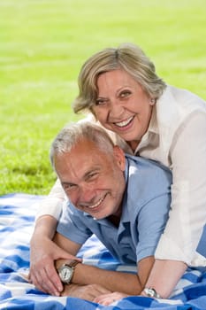 Active retirement laughing senior couple lying in grass