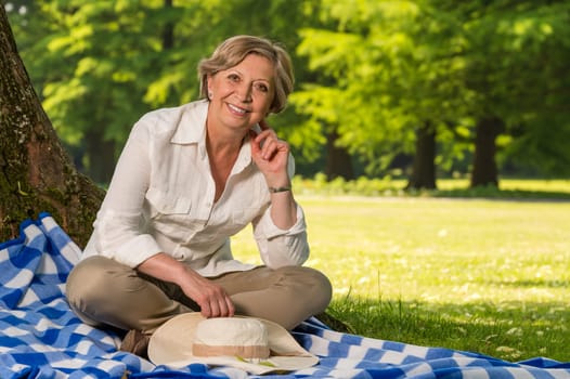 Portrait of senior woman sitting on blanket in park