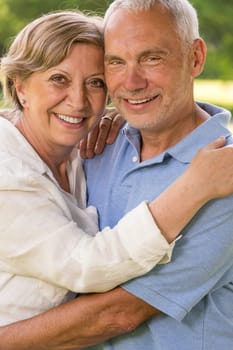 Senior couple hugging and smiling in park looking at camera