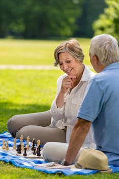 Elderly friends couple playing chess in park on sunny day