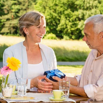 Senior woman giving husband anniversary gift in park