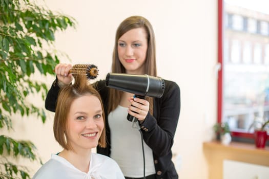 Hairdresser with a barrel brush and a blow-dryer styling a customers hair