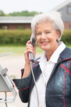 Smiling elderly woman at a telephone booth
