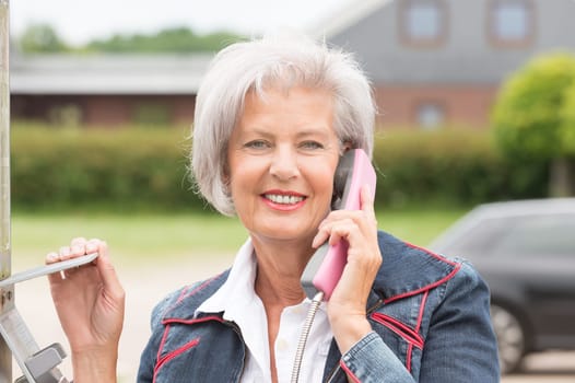 Smiling elderly woman at a telephone booth