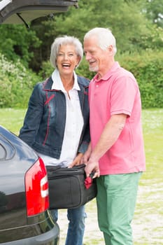 Senior couple loading a car with a suitcase