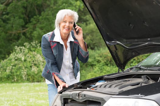 Senior citizen with mobile phone at a car with an open hood