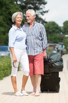 Happy senior couple with suitcases on a sidewalk