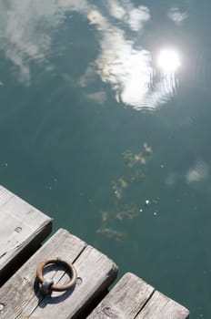 Reflection in the water of the sun and clouds and a wooden jetty