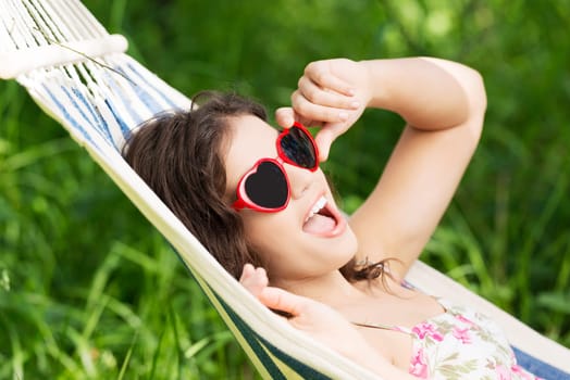 young woman lying in a hammock in the garden with heart shaped sunglasses.