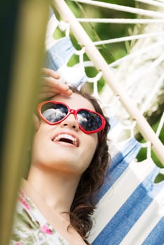 young woman lying in a hammock in the garden with heart shaped sunglasses.