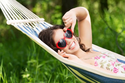 young woman lying in a hammock in the garden with heart shaped sunglasses.