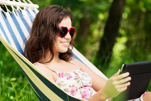 young woman lying in a hammock in the garden with e-book on tablet computer.