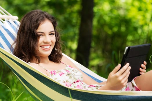young woman lying in a hammock in the garden with e-book on tablet computer.