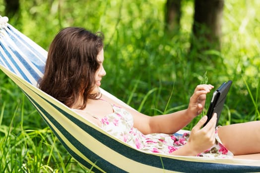 young woman lying in a hammock in the garden with e-book on tablet computer.