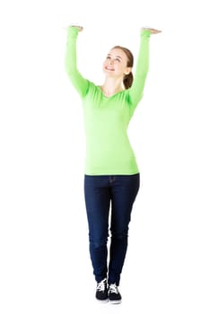 Smiling young woman is holding something abstract above her head. Happy girl with raised hands. Isolated on white background.