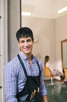 portrait of young male hairstylist standing out of shop and looking at camera