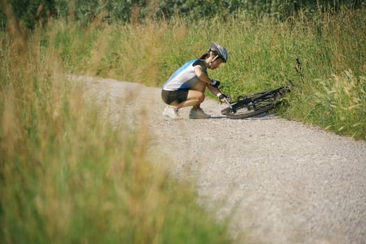 young woman training on mountain bike and repairing flat tyre on track in countryside