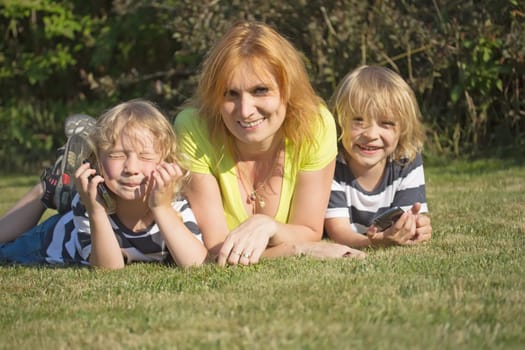 Mother with her blond hair sons is lying and smiling on the lawn in the garden.