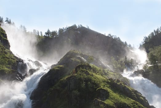 two waterfalls in the sun with trees around it