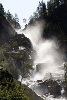 a wild waterfall in the sun with forest surrounding it