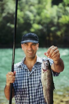 mid adult fisherman on holidays on river, relaxing and fishing trout. Focus on fish