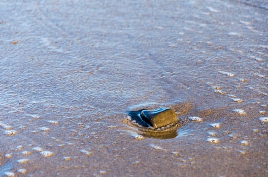 A single wet rock at the beach surrounded by sand