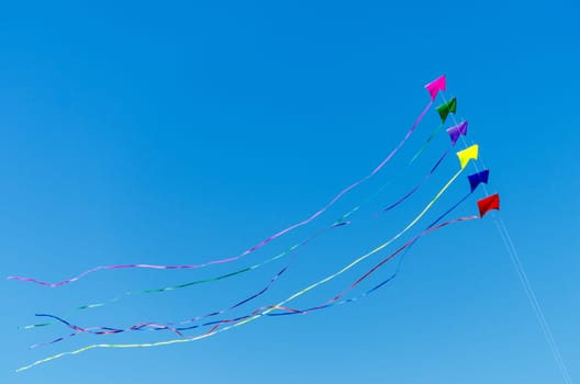 Rainbow colored kites flying against a beautiful blue sky