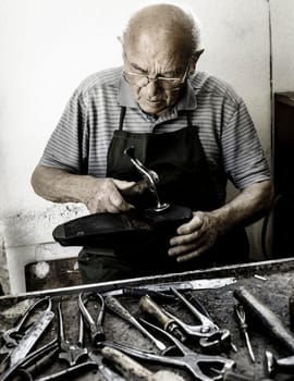 Old shoemaker repair the sole of a shoe.