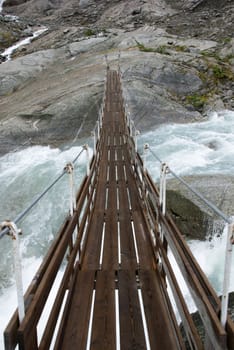 a small plank bridge leading over a torrential river