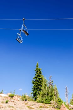 Ski lift with a deep blue sky passing over green pine trees in the summer on Mount Hood