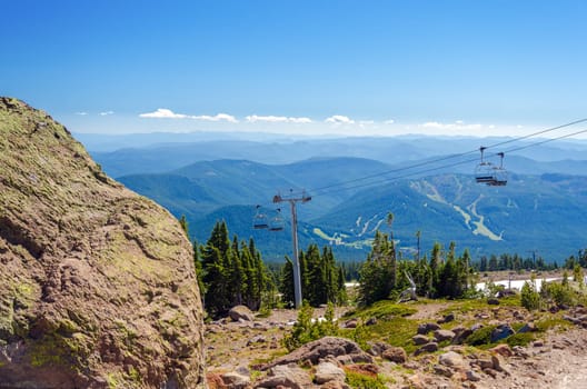 Chairlift going up Mount Hood with forest covered hills in the background and a large boulder in the foreground