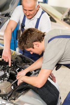 Middle aged car repairman helping colleague in garage