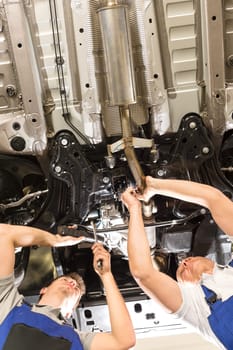 Caucasian repairmen working under lifted automobile