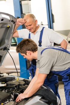 Elderly mechanic supervising young colleague's work