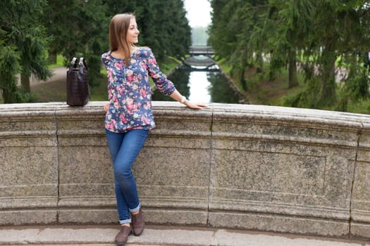 Beautiful young girl on the old stone bridge in the coniferous forest