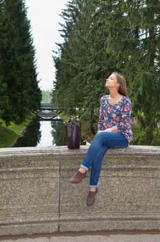 eautiful girl sits on an old stone bridge in the coniferous forest