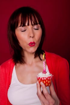 A beautiful woman is blowing out a candle on a cupcake and making a wish for her birthday.