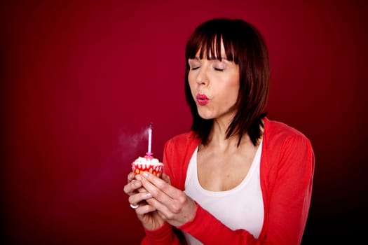 A beautiful woman is blowing out a candle on a cupcake and making a wish for her birthday.