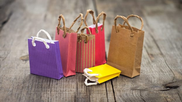 Colorful miniature paper shopping bags on wood background.