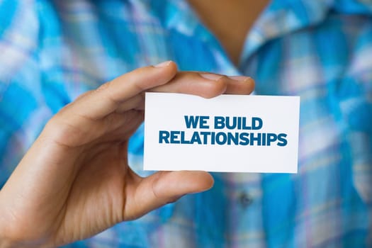 A person holding a white card with the words We build Relationships