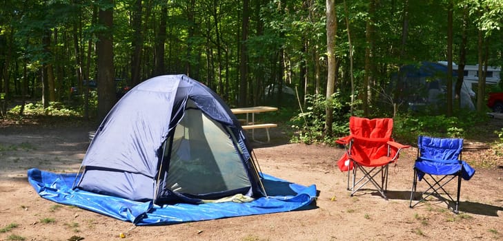 Campsite with chairs and tent among trees